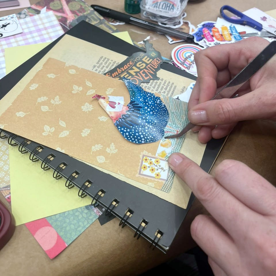 Participante decorando una página de su libreta con papeles con diseño y pinzas en el taller de journaling